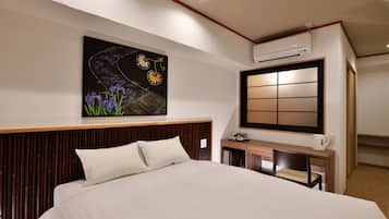 Habitación de hotel con una cama grande, un escritorio con silla, aire acondicionado de pared y un cuadro de flores.