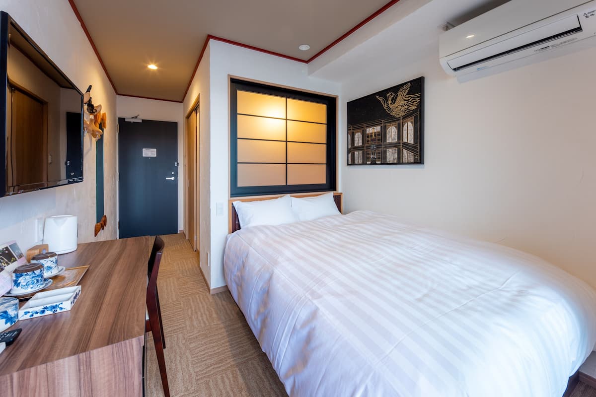 Een hotelkamer met een bed, bureau, stoel, spiegel, airconditioning en een deur.