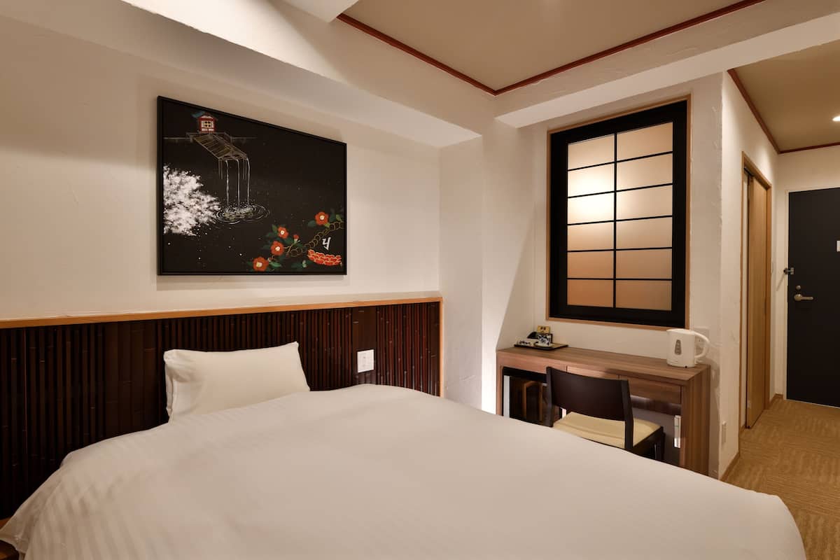 Een hotelkamer met een groot bed, een bureau met een stoel, een kunstwerk aan de muur en een schuifdeur.
