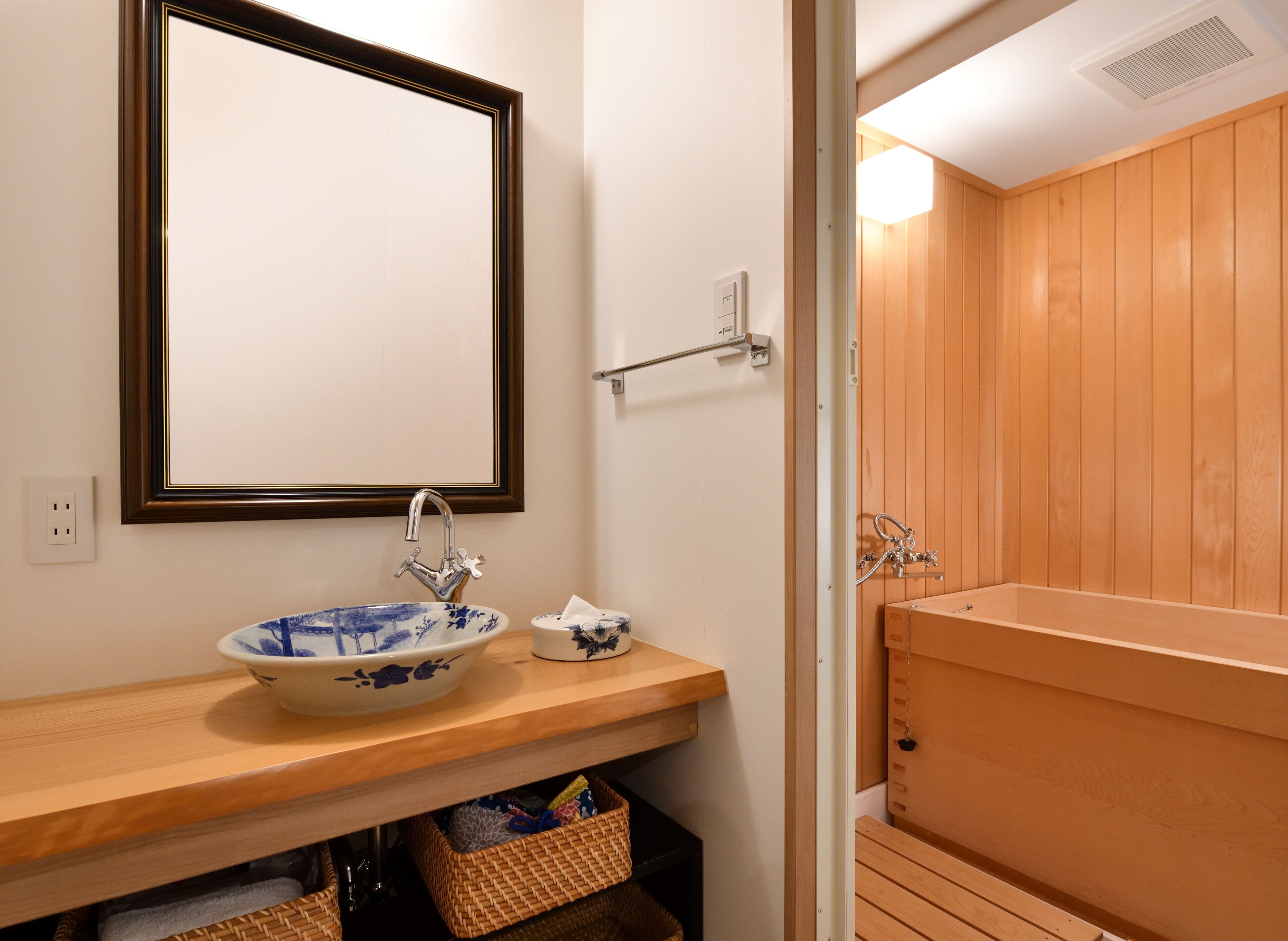 Een badkamer met een houten wastafelmeubel, een keramieken wastafel in blauw en wit, en een houten bad.