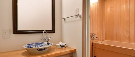 A bathroom with a wooden vanity, a blue and white ceramic sink, and a wooden bathtub.