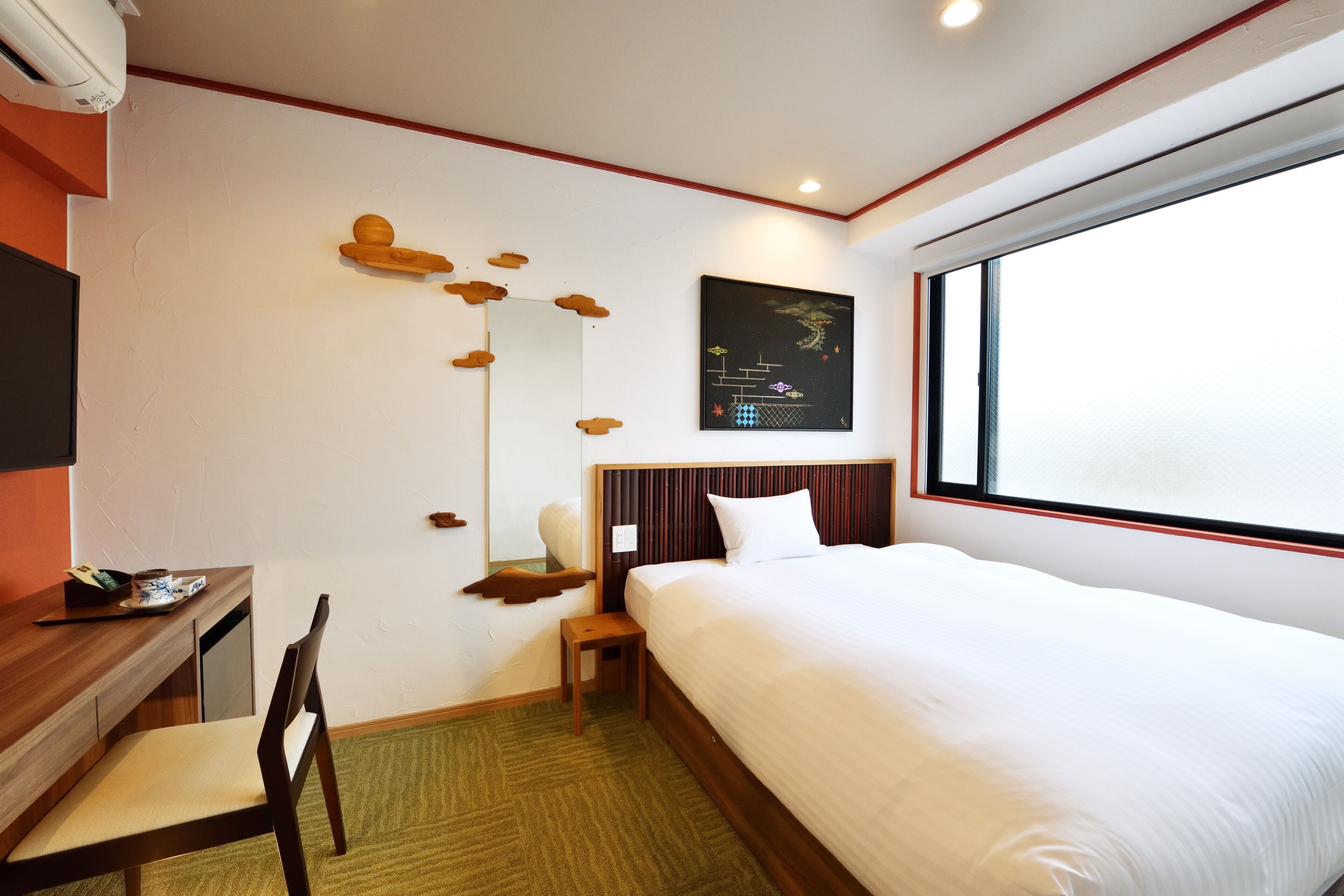 A hotel room with a bed, desk, chair, and a window.