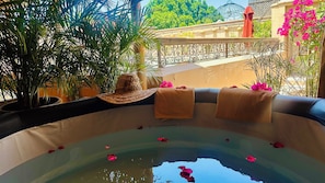 A hot tub with rose petals, a straw hat, and towels on a balcony with a view of greenery and a building. - Riad  Dar Eternity (Marrakech)
