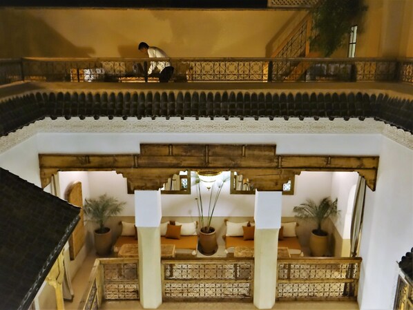 A traditional courtyard with a wooden bench, potted plants, and a balcony with a railing.