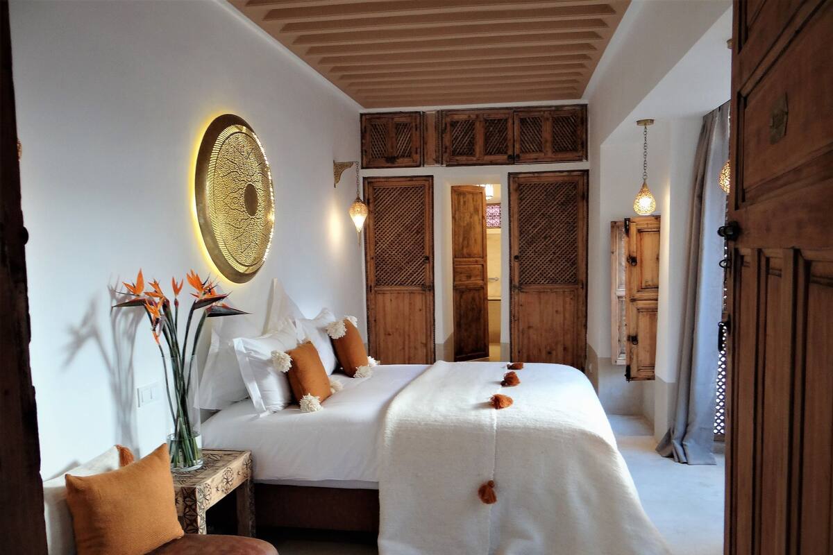 A hotel room with a large bed, wooden doors, and a decorative wall piece.