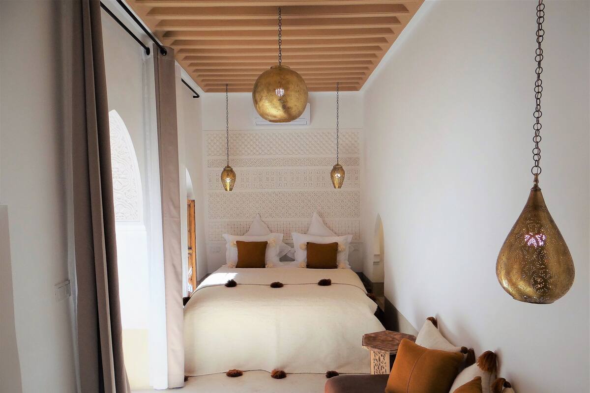 A bedroom with a bed, pillows, a hanging light fixture, and a small wooden table.