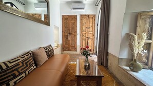 Una sala de estar con un sofá, una mesa de centro y un jarrón con flores. Hay dos puertas de madera y una ventana con cortinas.