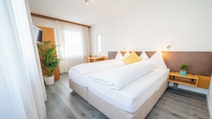 Een moderne hotelkamer met een groot bed, een nachtkastje, een plant in pot en een spiegel.