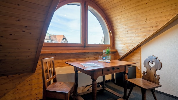 Een houten interieur met een groot gewelfd raam, een houten tafel, twee stoelen en een klein kastje.