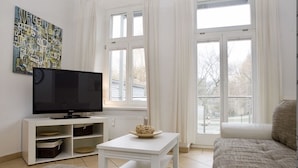 Ein Wohnzimmer mit einem Flachbildfernseher auf einem weißen Schrank, einem weißen Couchtisch mit einer Schale und einem beigen Sofa.