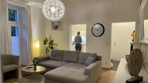 Ein modernes Wohnzimmer mit einer Eckcouch, einem runden Couchtisch, einer Topfpflanze, einer dekorativen Leuchte und einer Wanduhr.