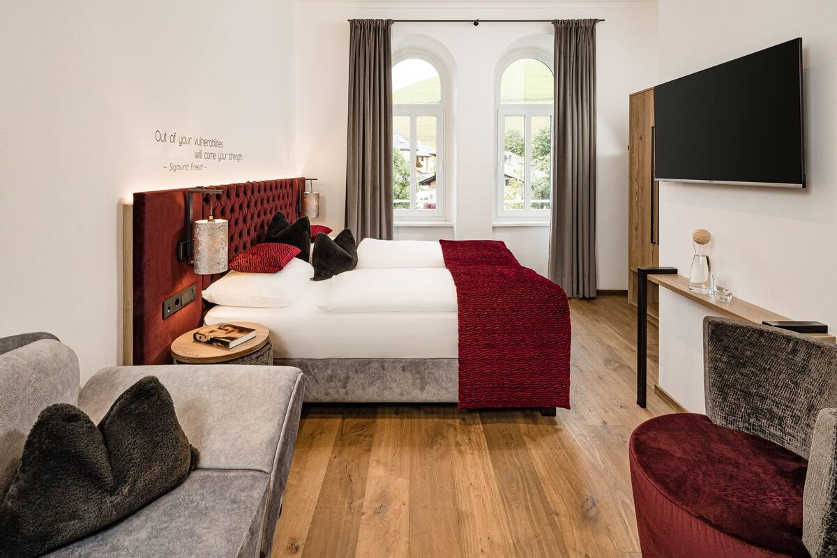 Et moderne hotelværelse med seng, fjernsyn, et lille bord og et vindue med gardiner.