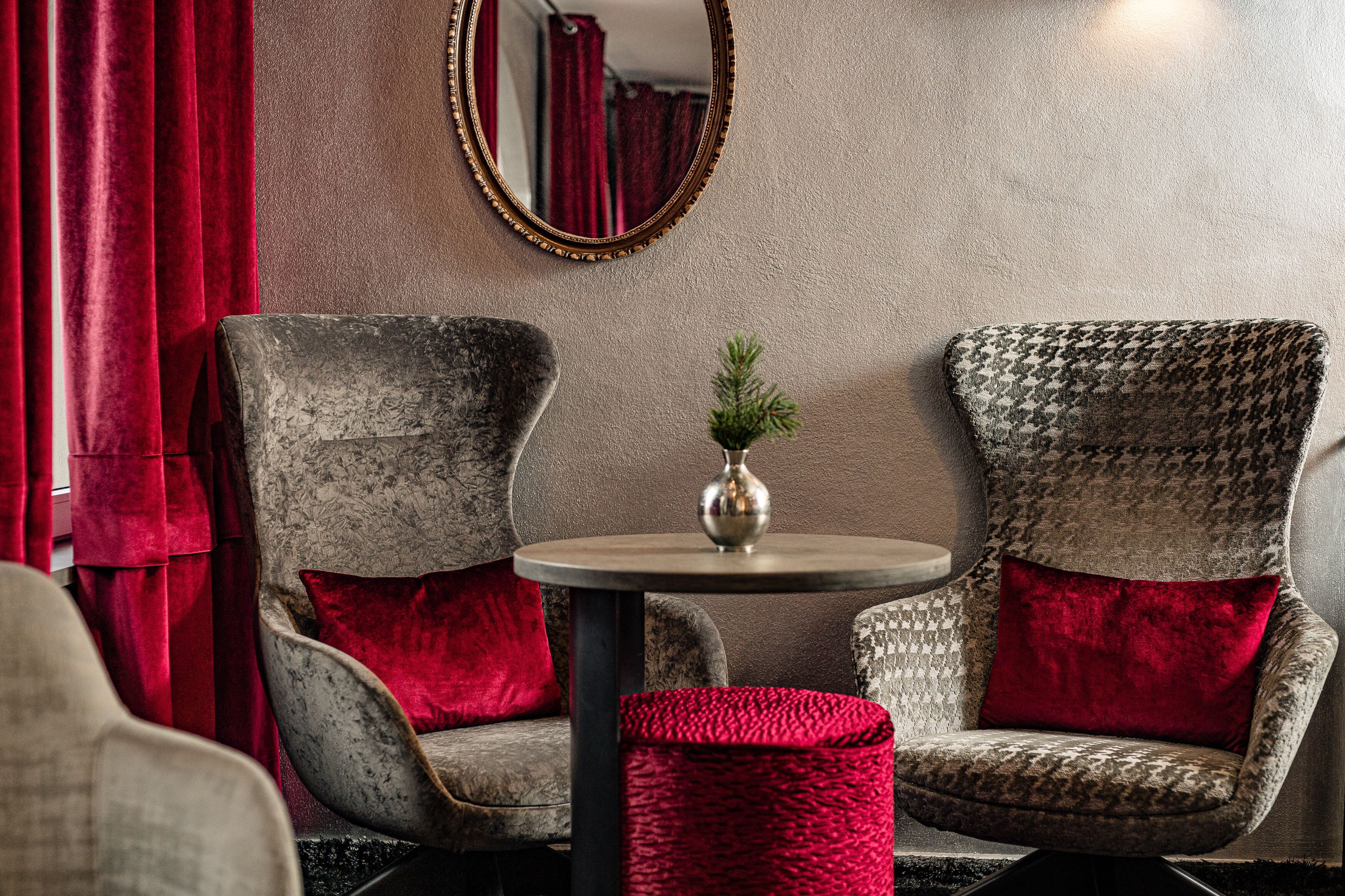 A room with two armchairs, a small round table with a vase, and a red curtain.