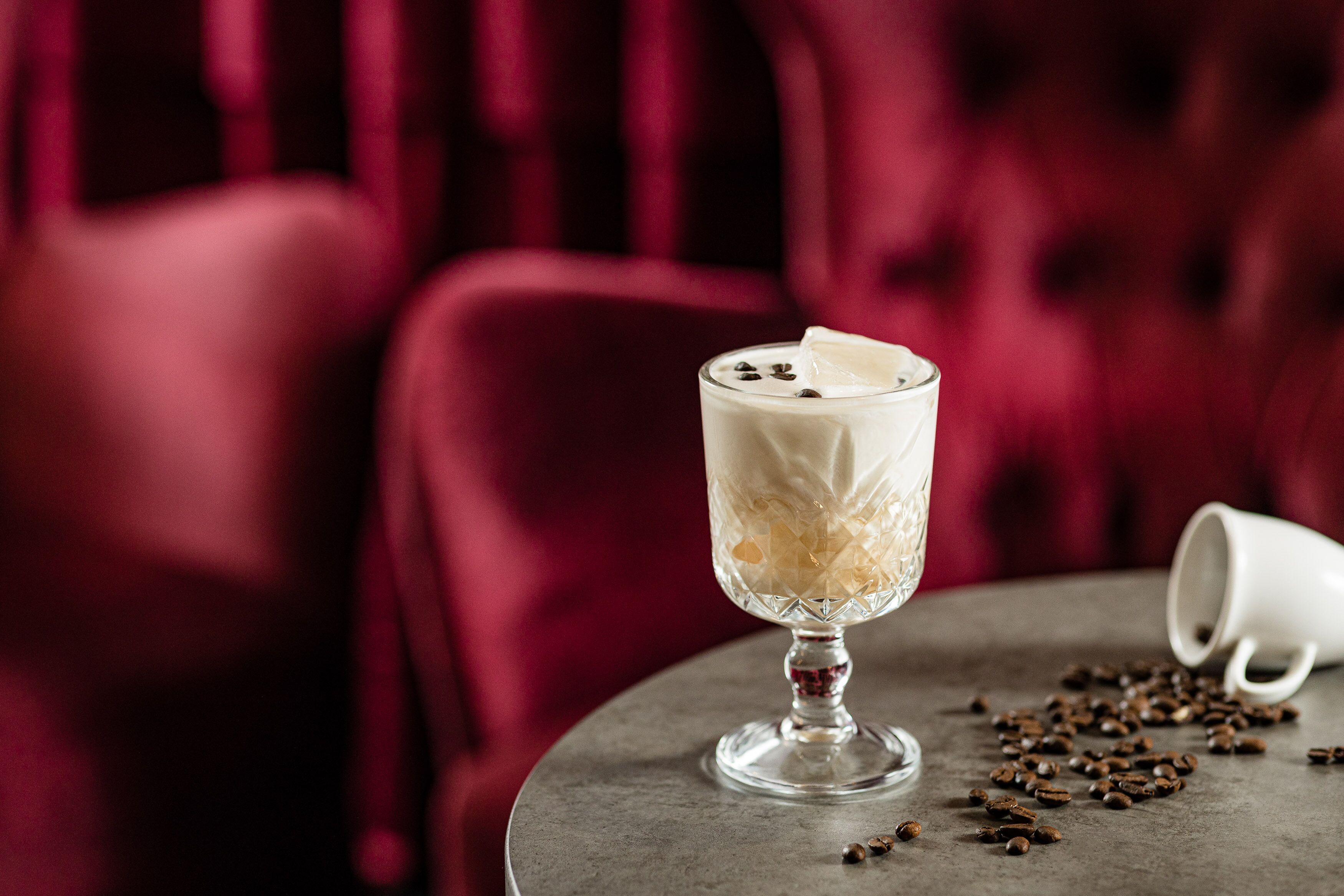A glass of iced coffee with whipped cream and chocolate chips on a table with scattered coffee beans.