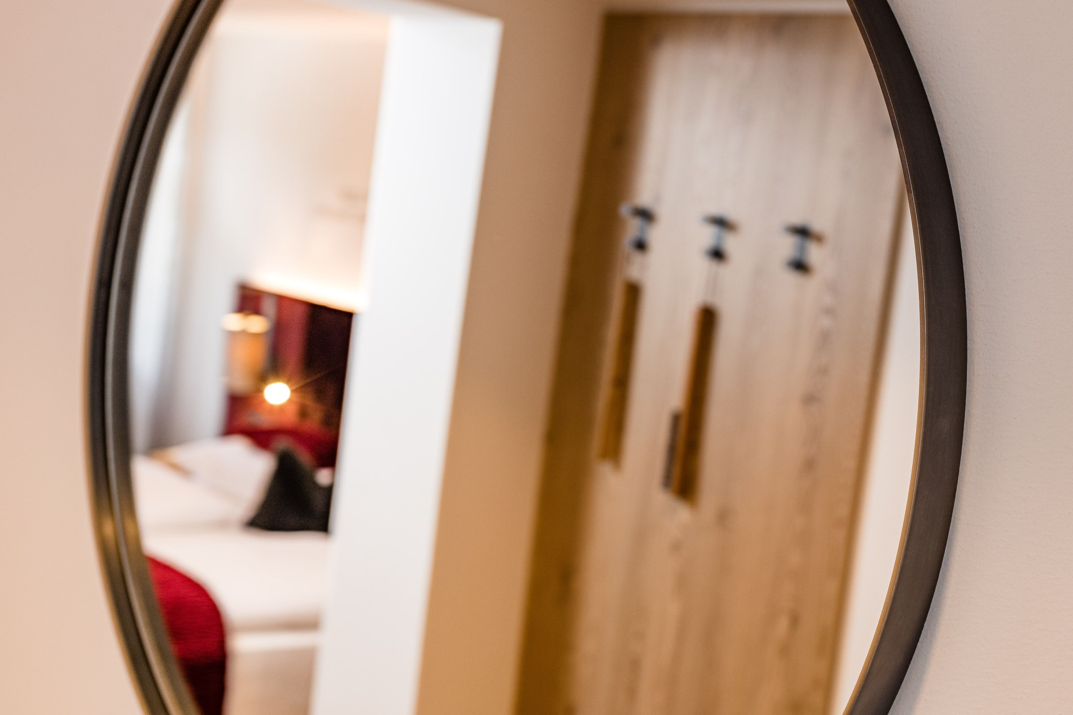 Un espejo refleja una habitación con una cama, un cojín rojo y una puerta de madera con tres pomos.
