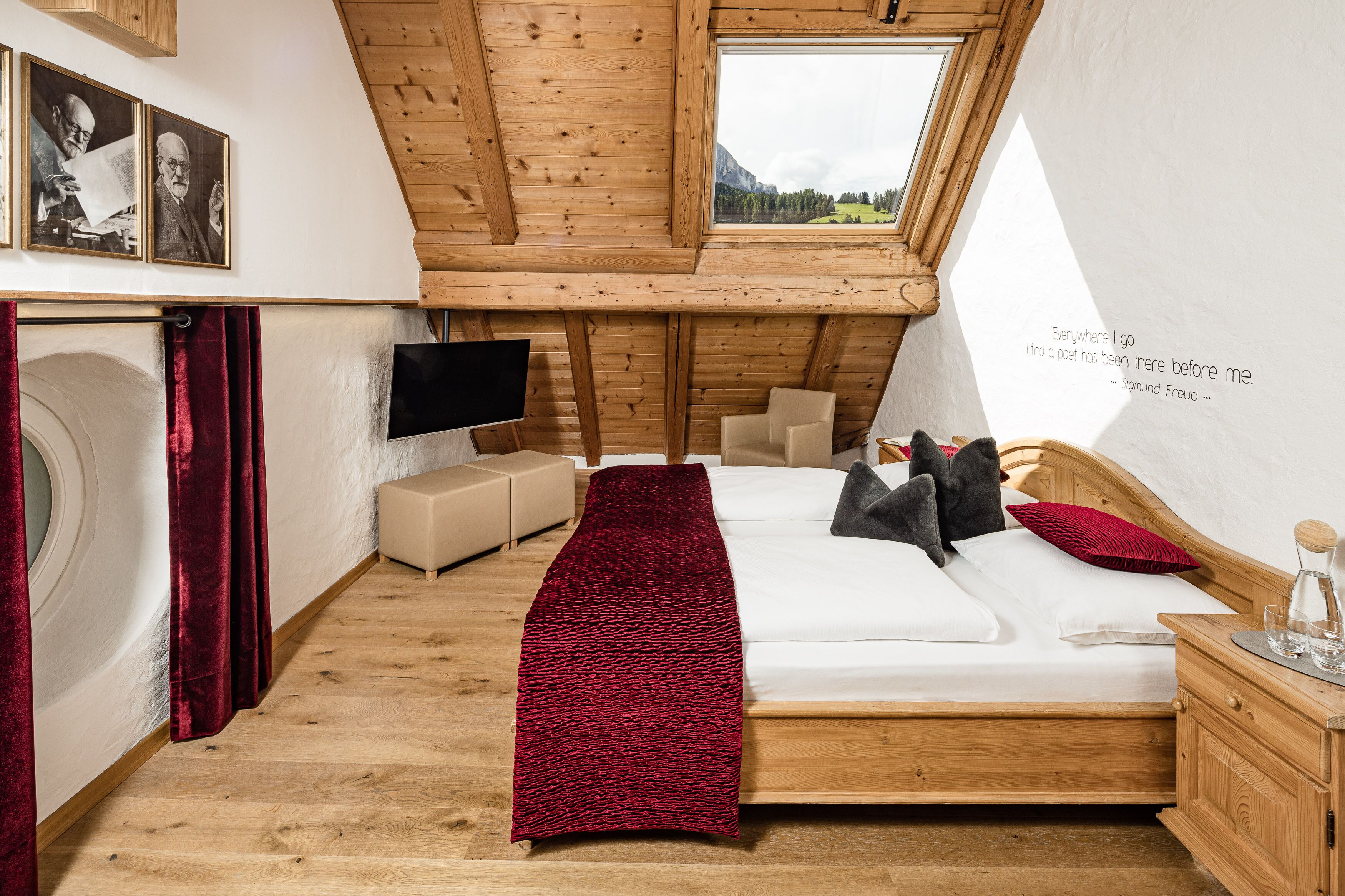 A bedroom with a wooden ceiling, a bed with pillows, a TV, a red blanket, and a quote on the wall.