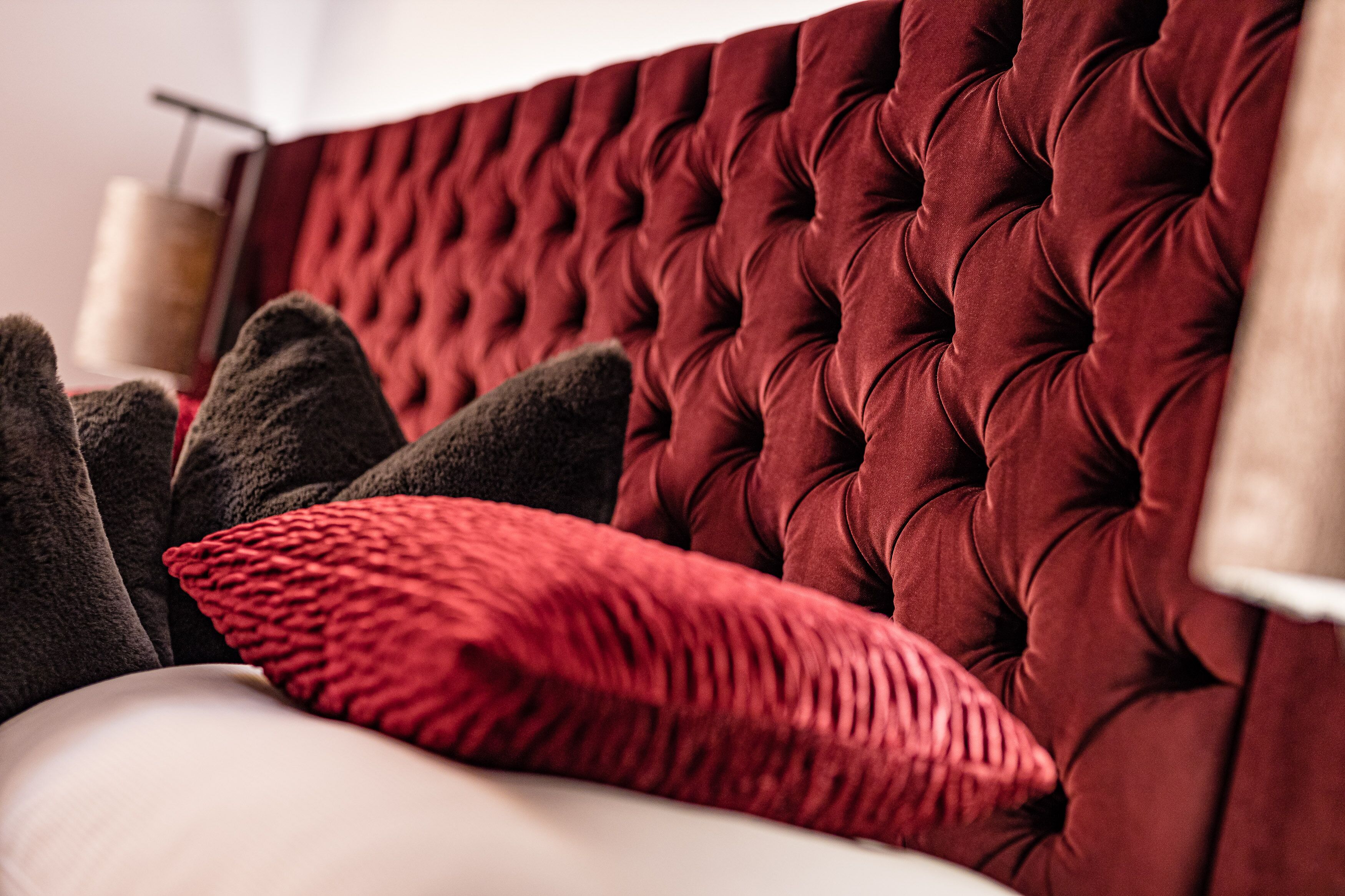 A tufted headboard with a plush texture, accompanied by a dark and a red pillow on a white surface.