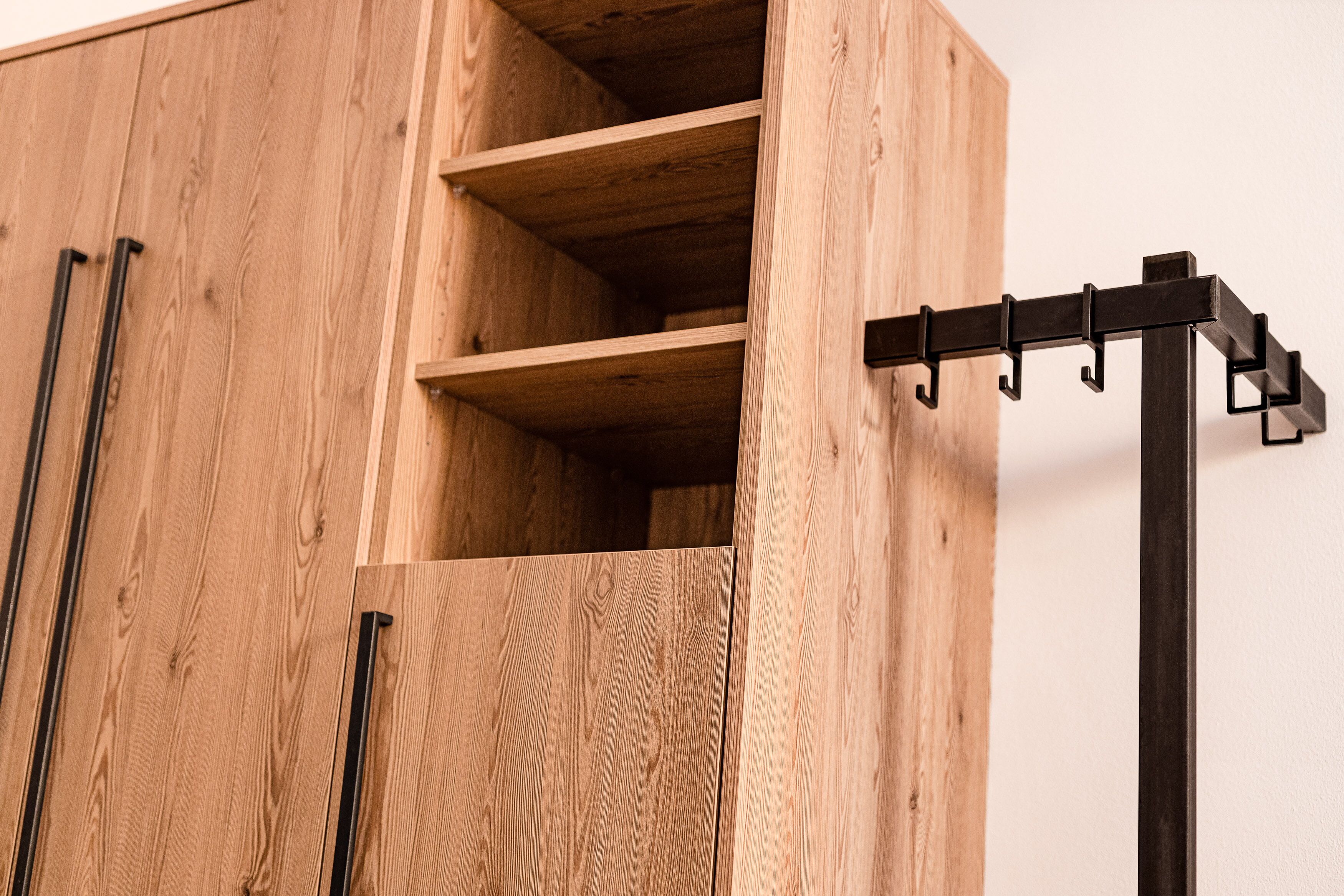 A wooden cabinet with multiple compartments and a black metal rack with hooks.