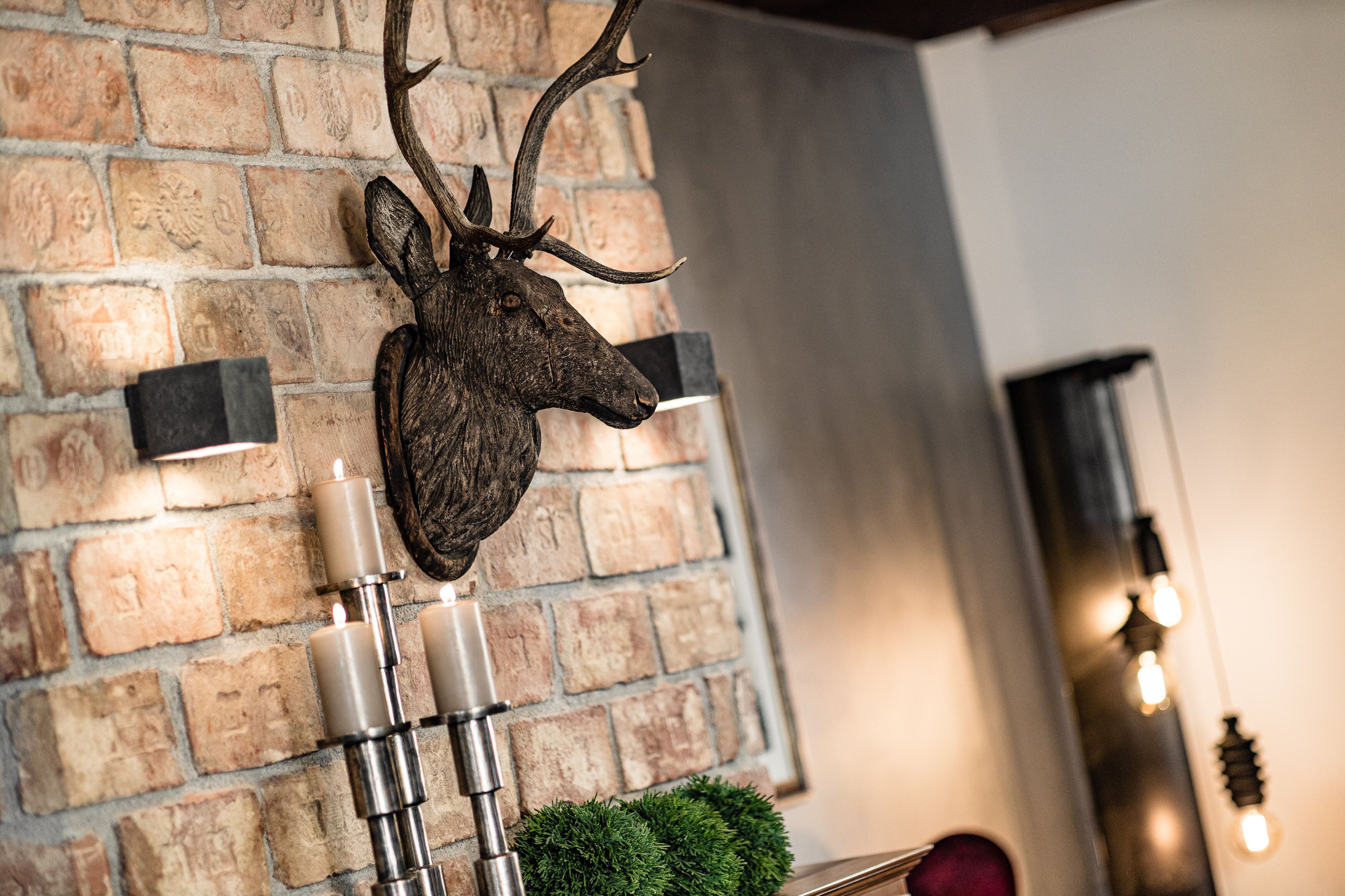 A deer head mounted on a brick wall, accompanied by candles and a small green plant.