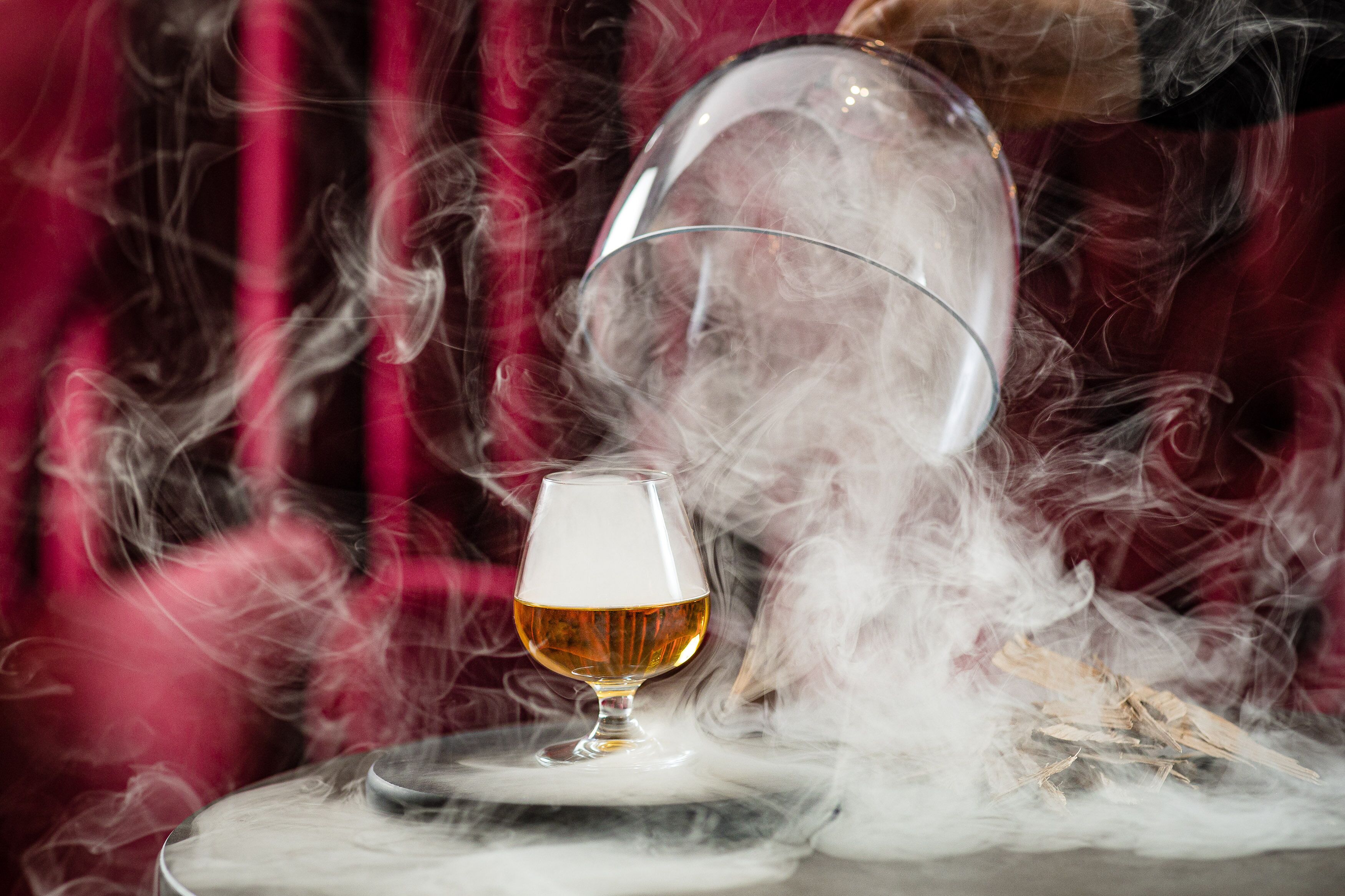 Un vaso de líquido ámbar sobre una mesa, rodeado de humo.
