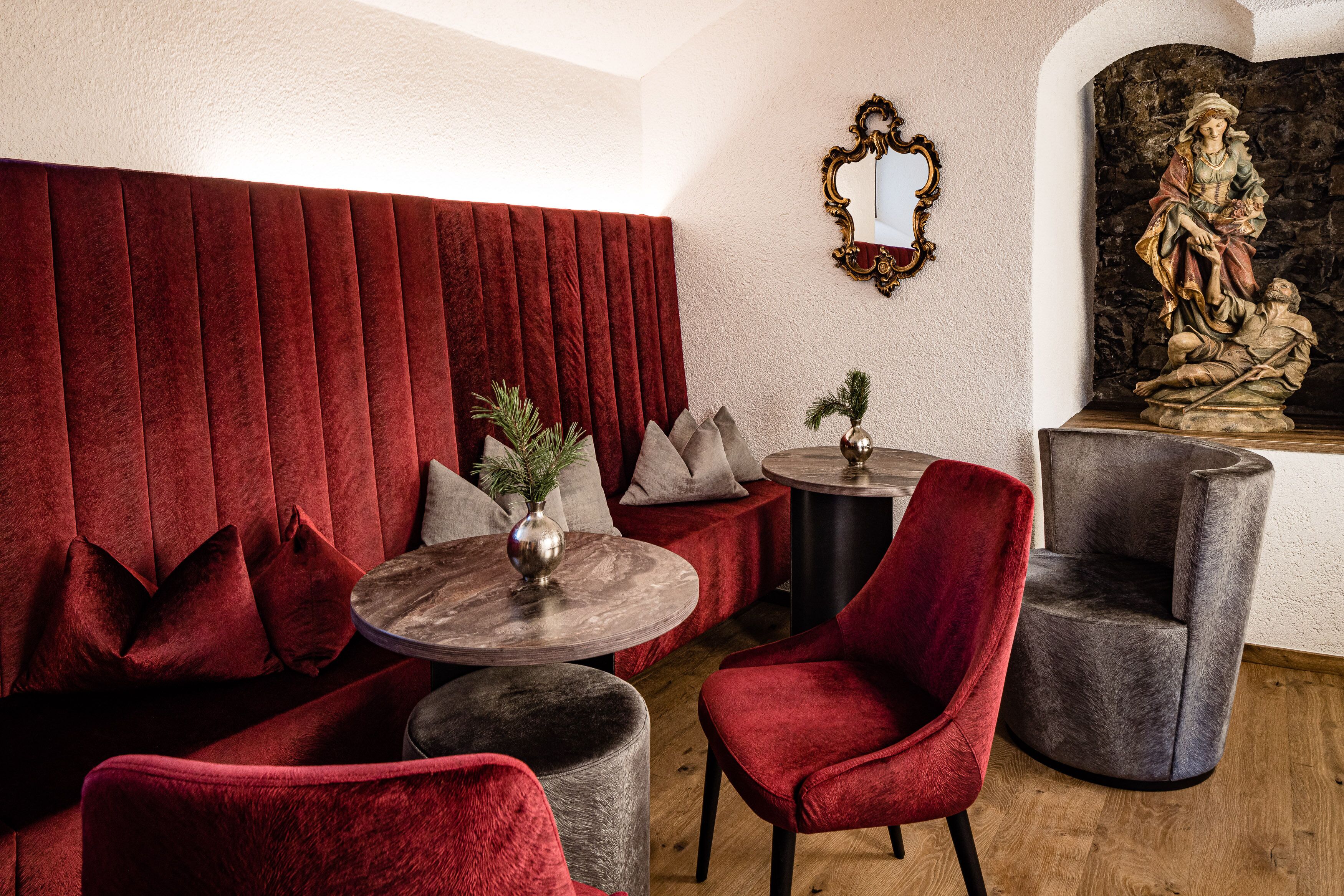 A room with a red velvet sofa, a round wooden table, and two grey armchairs.
