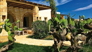 A rustic building with a stone facade, a wooden pergola, and a cactus garden in the foreground.