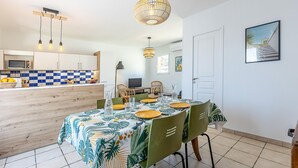 A dining area with a table set for four, surrounded by chairs. A kitchen with a microwave and a fruit bowl is visible in the background. - 2 bedroom awesome home in Serignan (Serignan)
