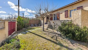 A courtyard with a stone pathway, a small tree, and a building with a red gate and windows. - 2 bedroom awesome home in Serignan (Serignan)
