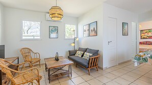 A living room with a sofa, two armchairs, a coffee table, and a dining table. There are two windows, a door, and a wall with framed pictures. - 2 bedroom awesome home in Serignan (Serignan)