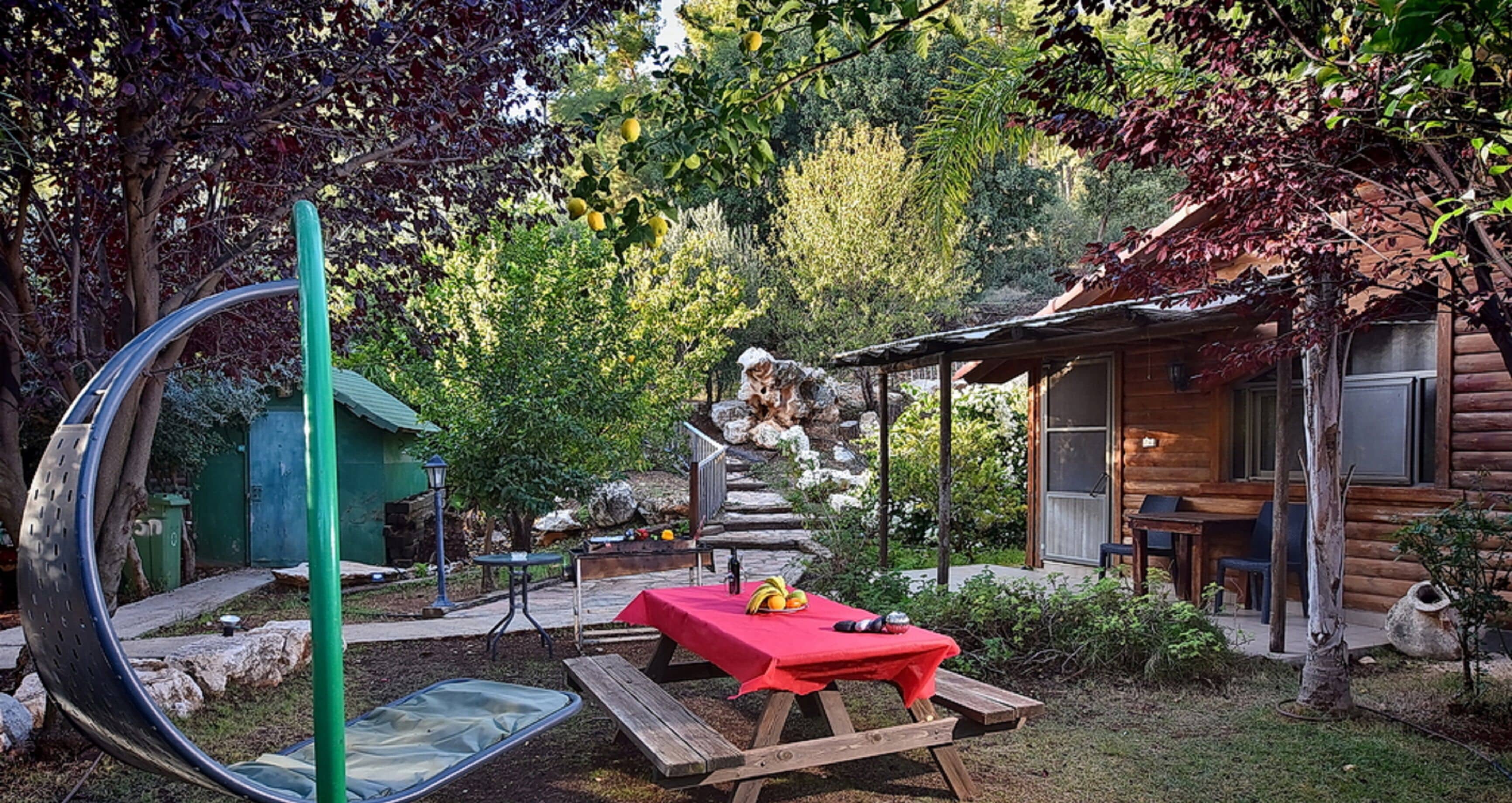 Un'area pranzo all'aperto dallo stile rustico, con tovaglia rossa, una panca di legno e un tavolo da picnic.