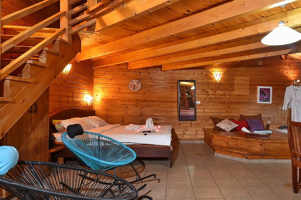Una cabaña de madera acogedora con una cama, una silla azul, una mesa de comedor con fruta y una escalera.
