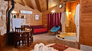 A cozy wooden cabin with a dining area, a red sofa, a blue chair, and a bathtub. - Niflaot Hagalil (Merom HaGalil)