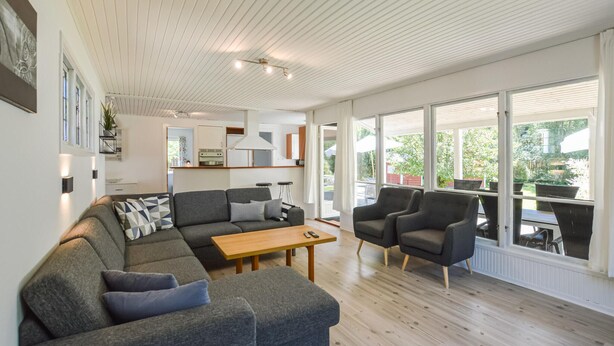 Una sala moderna con un sofá, sillones, una mesa de centro y una cocina al fondo.