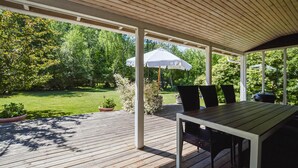Un patio techado al aire libre con piso de madera, una mesa, sillas y un paraguas blanco.