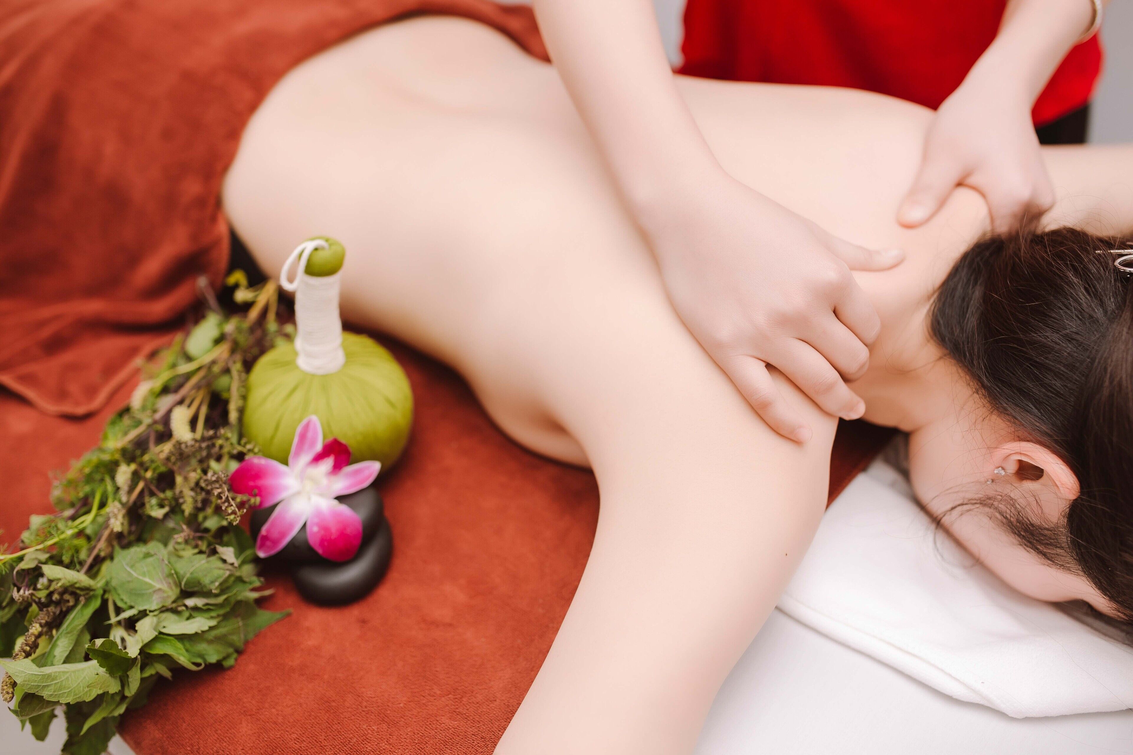 A person receiving a massage with a massage tool and herbs on a massage table.