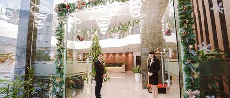 A hotel entrance decorated for Christmas with a 'Merry Christmas' sign, a Christmas tree, and festive garlands.