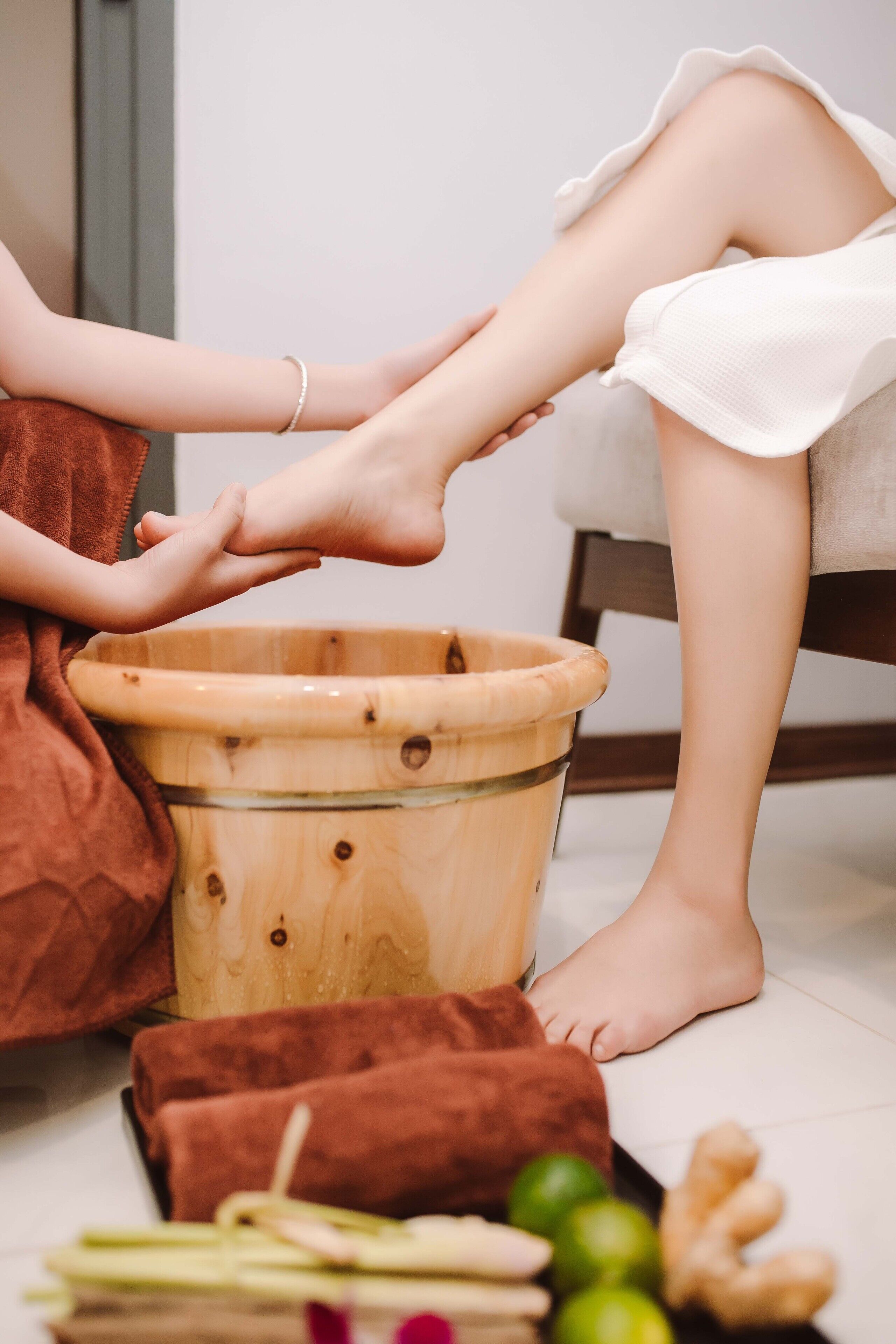 A person sitting on the floor with a wooden tub, a brown towel, and some ginger roots.