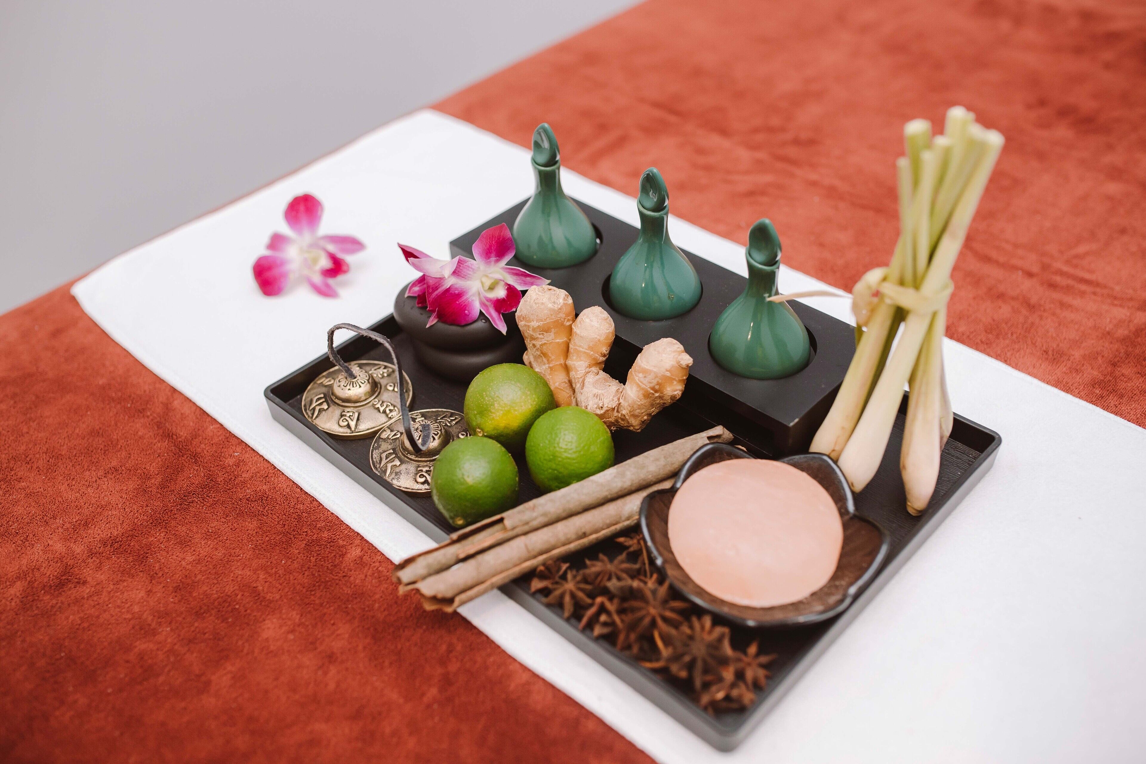 A tray with various items including a flower, ginger, cinnamon sticks, star anise, and a bowl of pink substance.