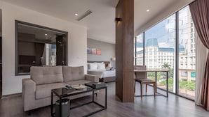 Quarto de hotel moderno com uma janela grande, um sofá, uma mesa de centro e um pequeno espaço de jantar.