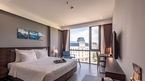 Quarto de hotel moderno com uma cama grande, uma mesa de trabalho, uma cadeira e uma televisão.