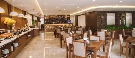 A modern hotel dining area with a buffet, wooden tables, and chairs.