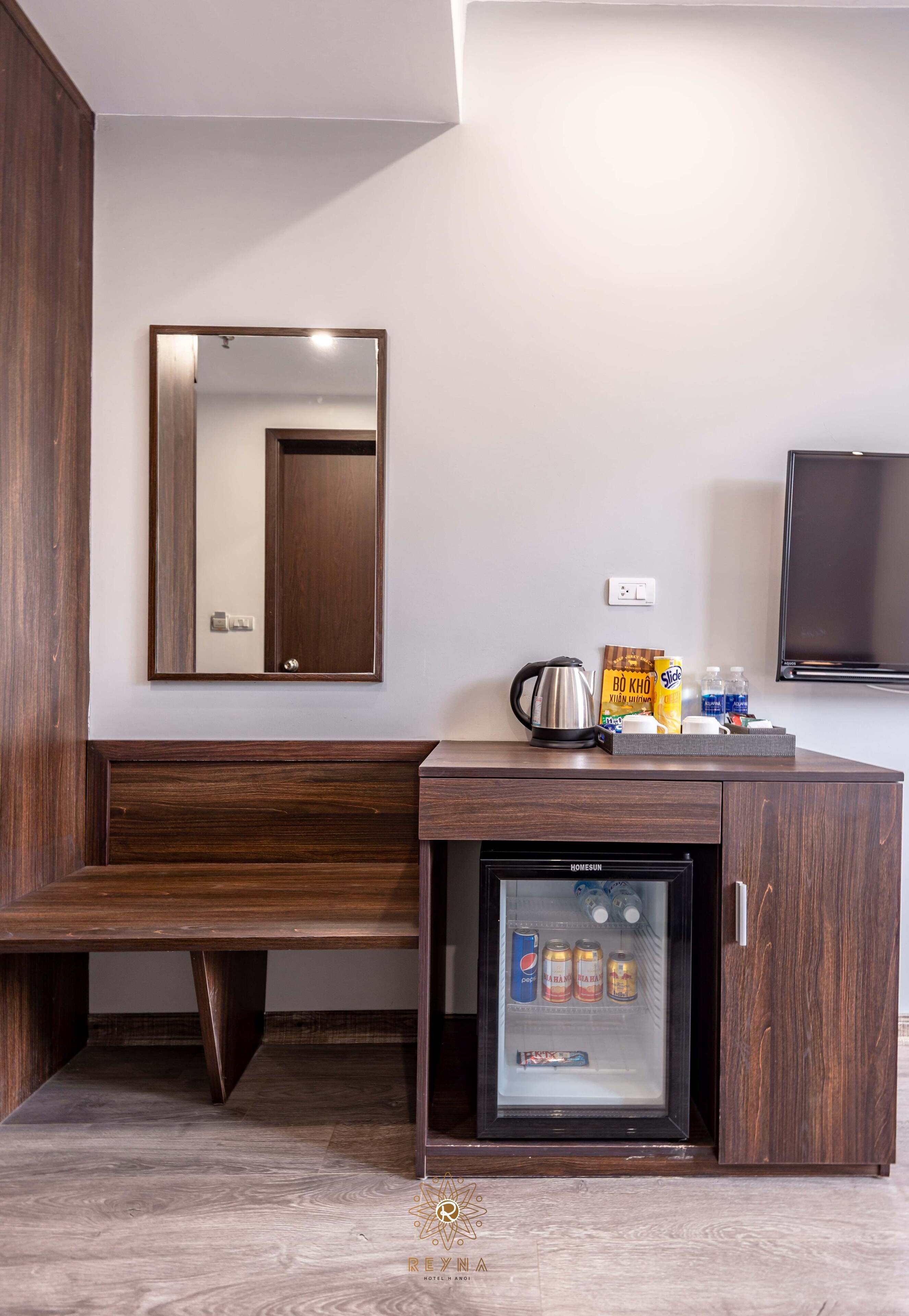 Habitación compacta con un banco de madera, un espejo, un minibar con bebidas y un televisor en la pared.