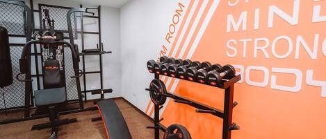 Un gimnasio con equipo de levantamiento de pesas, una banca y una pared con mensajes motivacionales.