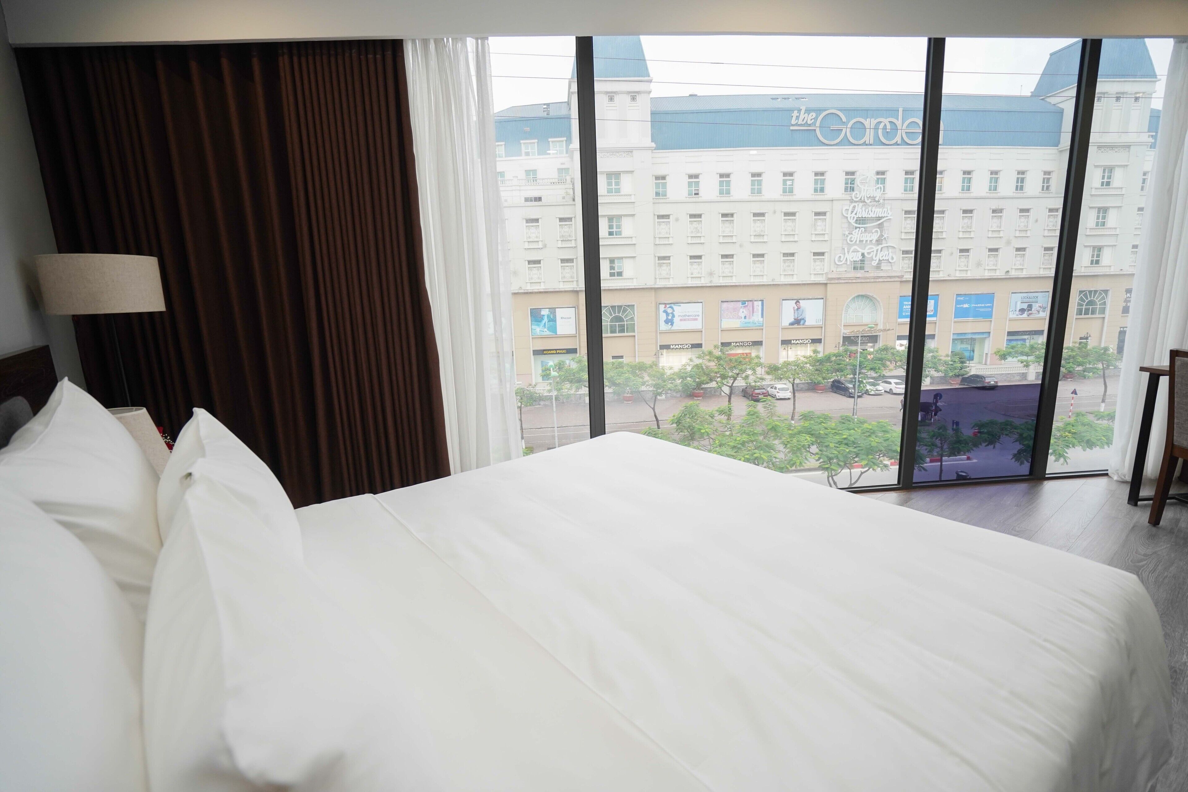 Una habitación de hotel con una cama grande, una lámpara y vistas a un edificio con el letrero "The Garden".