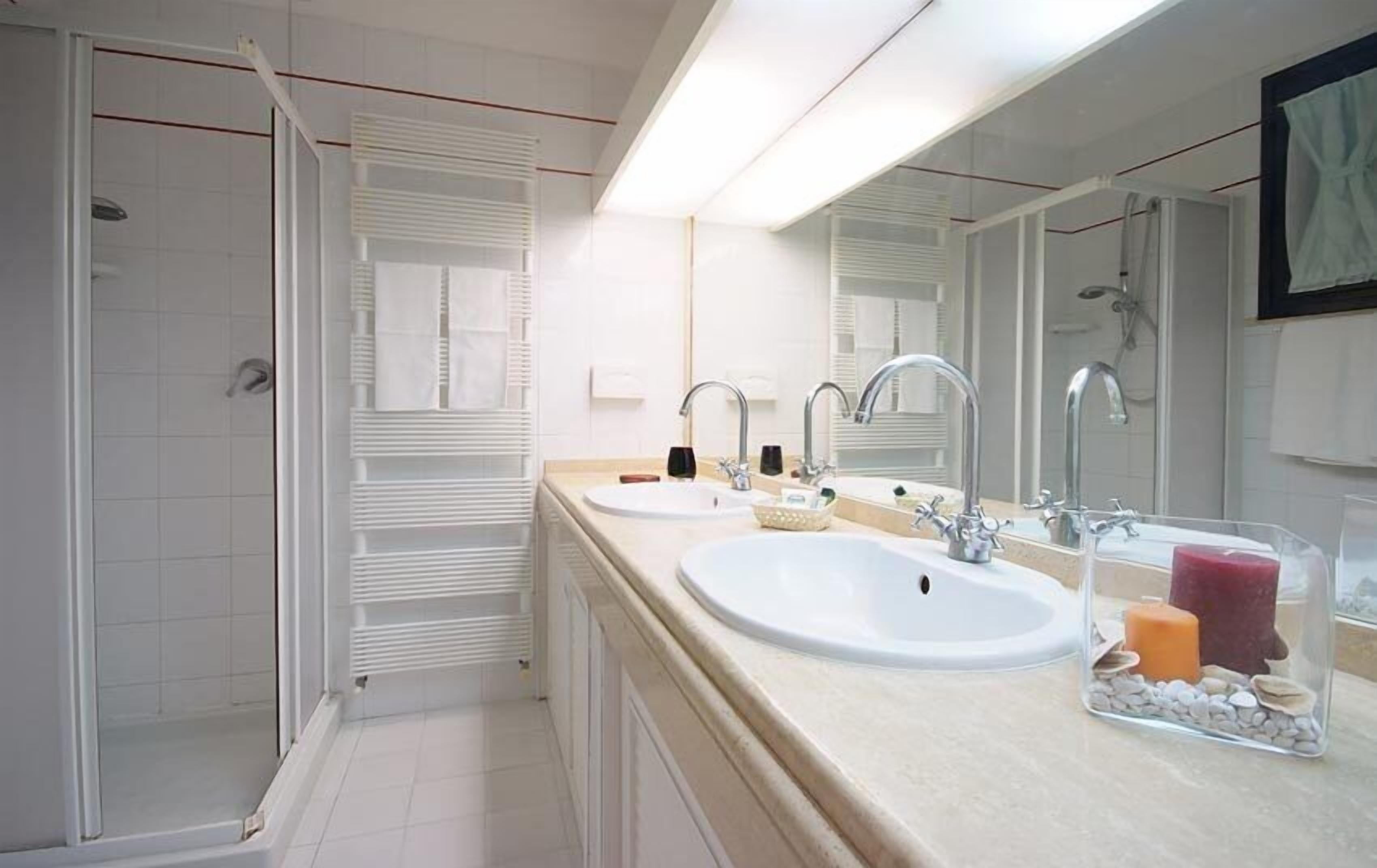 A modern bathroom with two sinks, a large mirror, and a walk-in shower.
