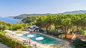A pool area with lounge chairs and umbrellas, surrounded by greenery and overlooking a body of water. - Hotel Valle Verde (Marciana)