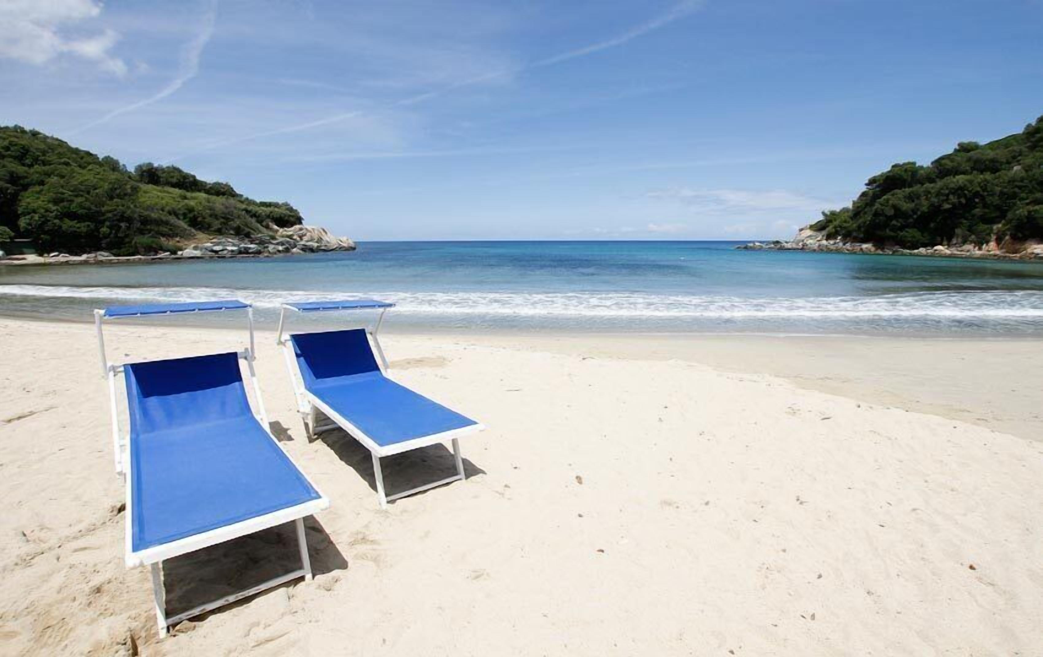 A beach with two blue lounge chairs and a sandy shore.
