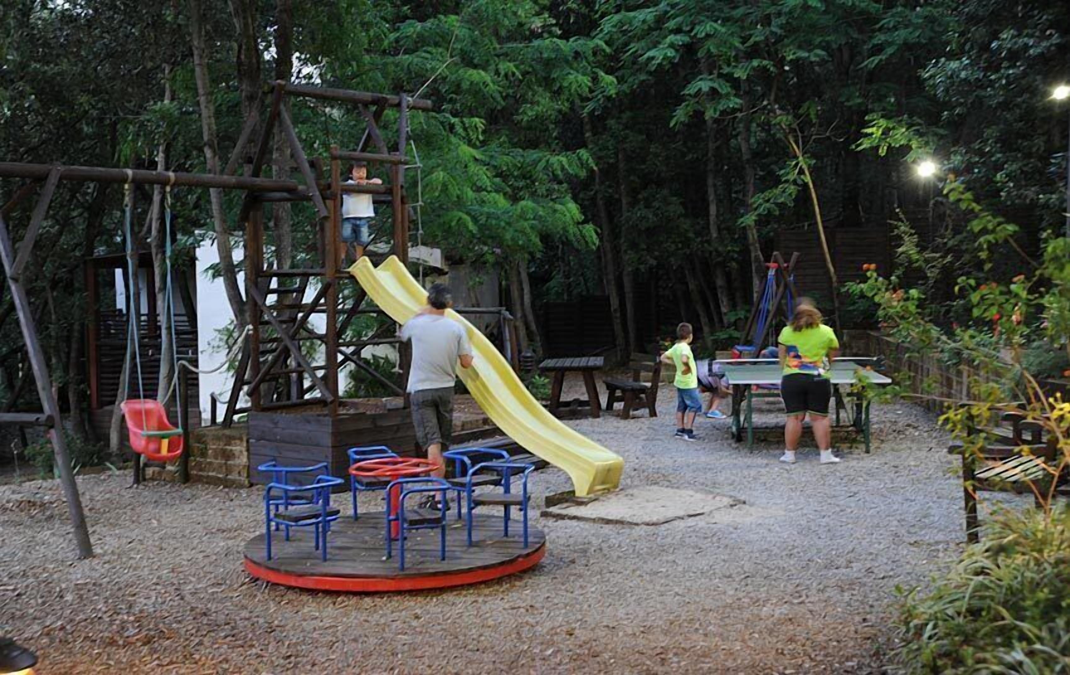 Ein Spielplatz mit Rutsche, Schaukeln und einer runden Sitzgruppe.
