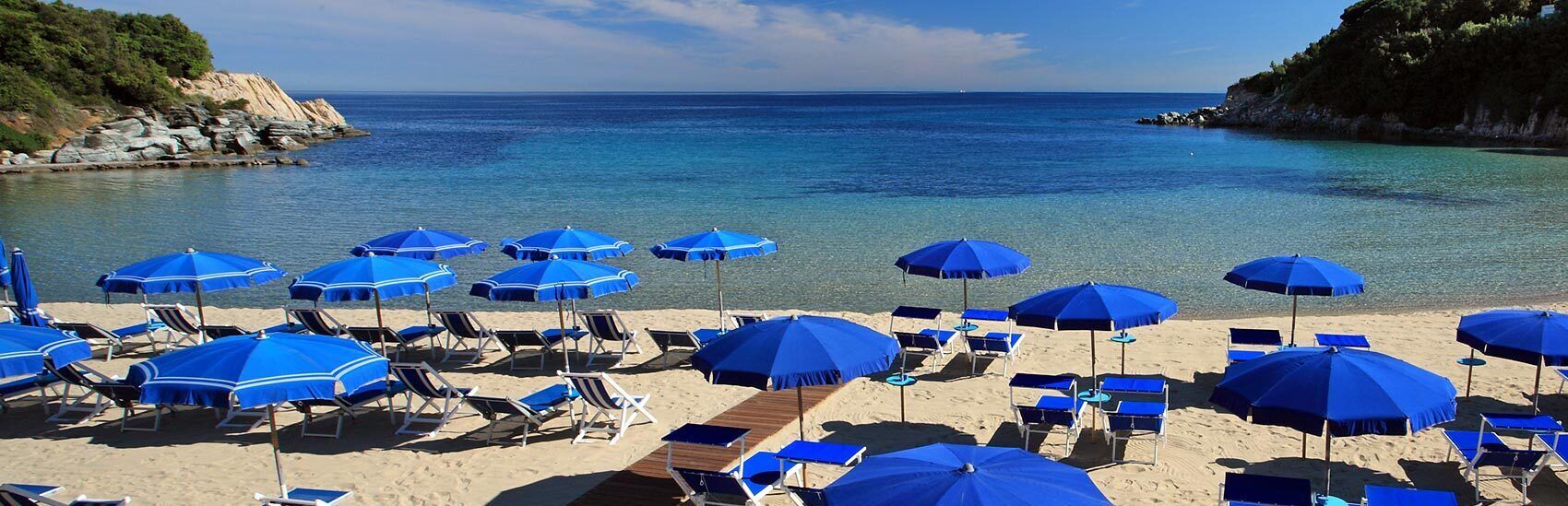 A beach with rows of blue umbrellas and sun loungers.