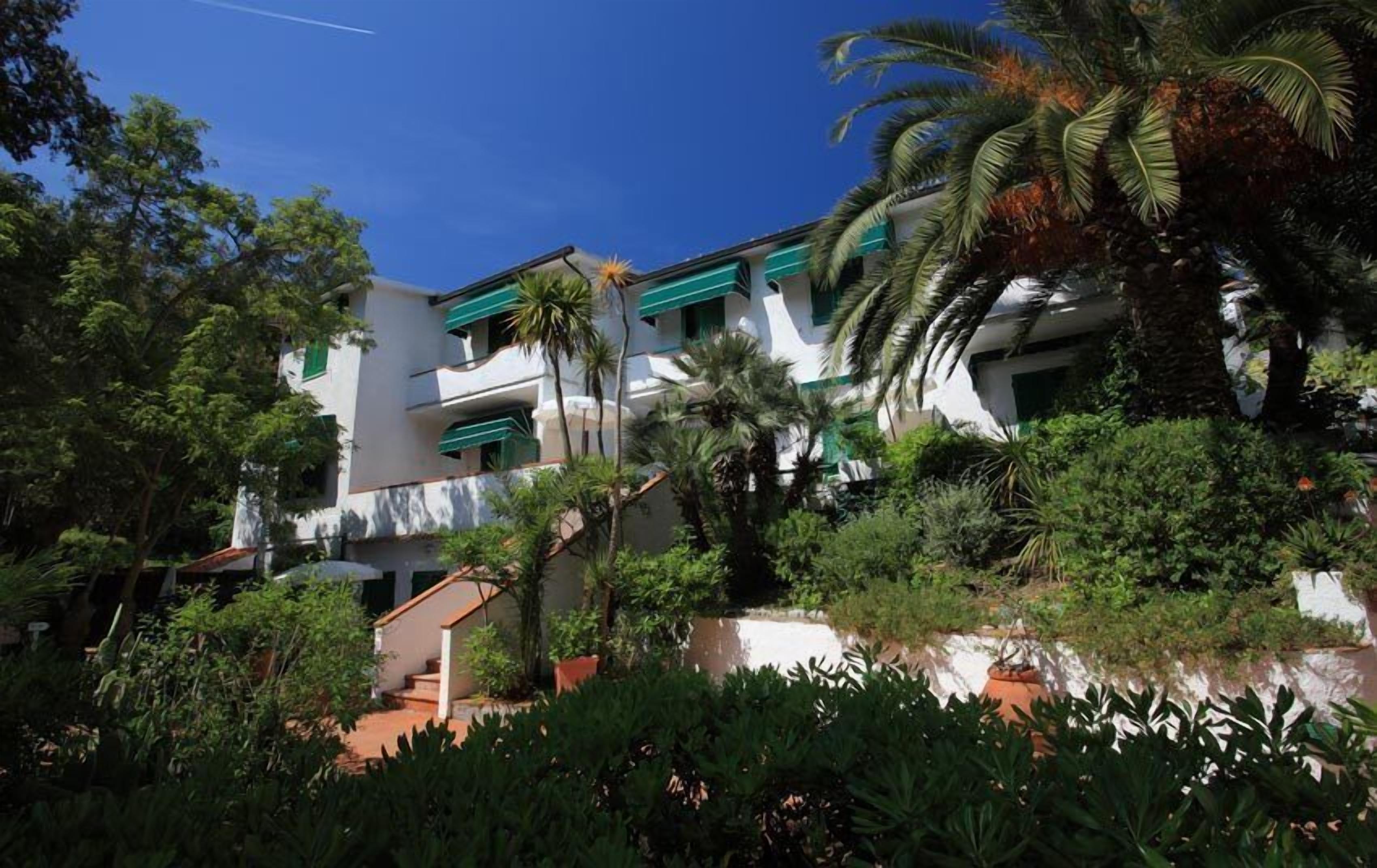 A multi-story building with balconies, surrounded by lush greenery and palm trees.